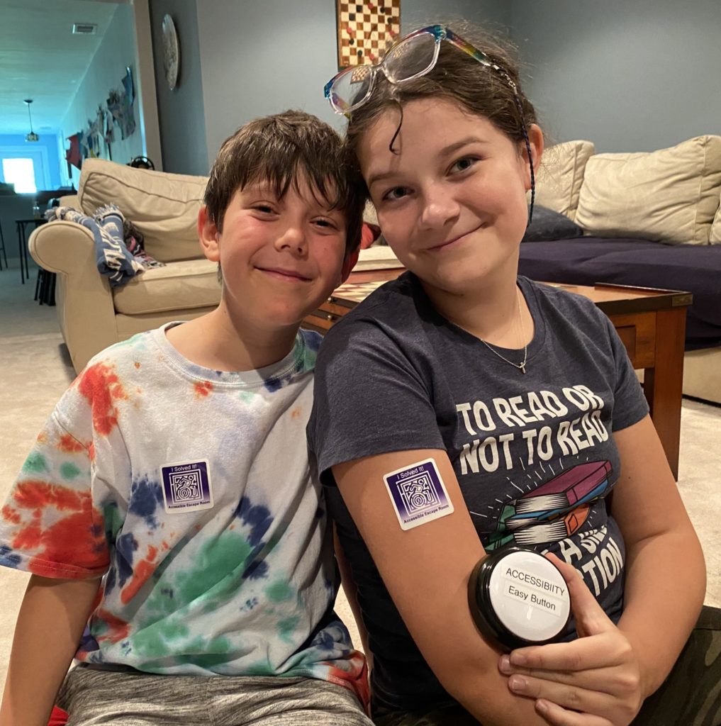 Two smiling kids with I solved the Accessible Escape Room stickers